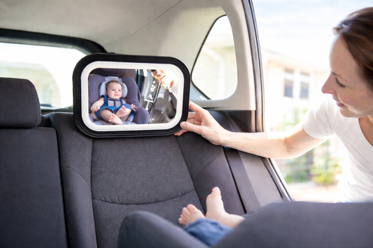 Mother adjusting a baby car mirror in the back seat, reflecting an infant secured in a rear-facing car seat inside a bright, modern vehicle interior.
