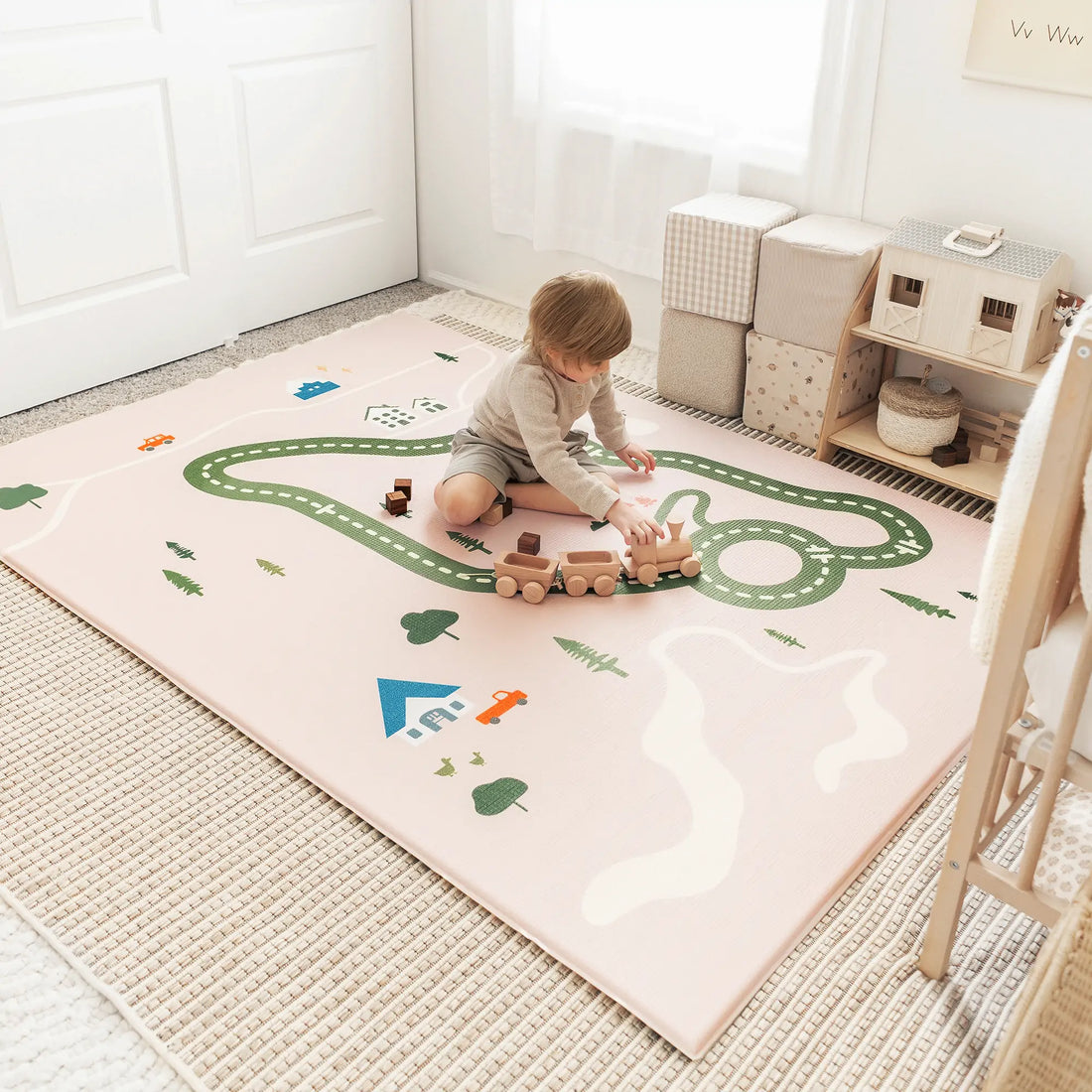 Toddler playing with wooden train toys on a soft road-pattern floor play mat in a bright neutral nursery.