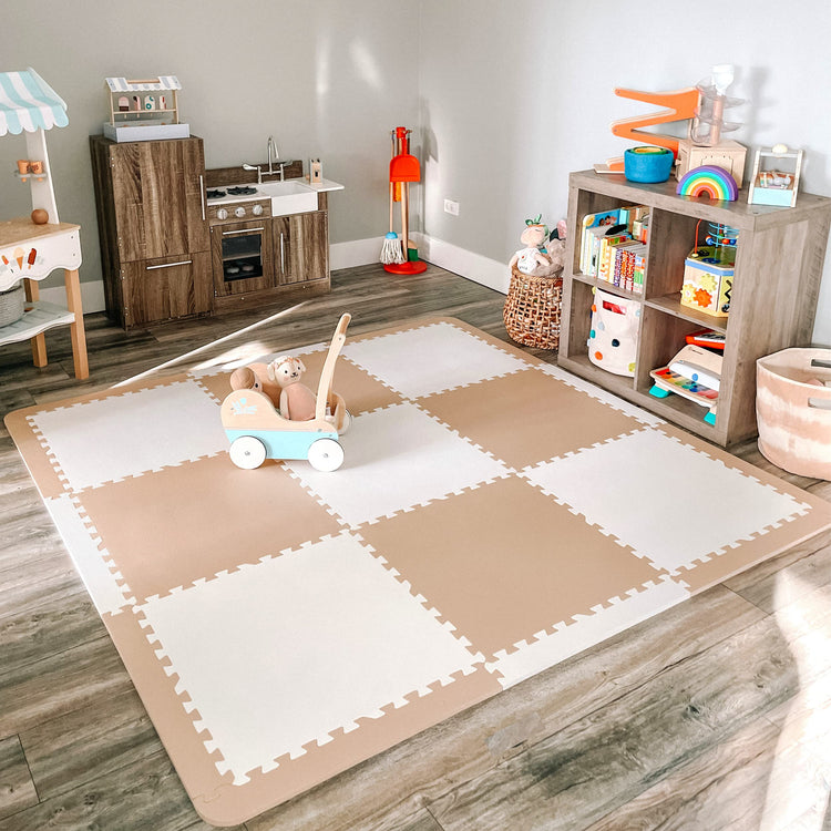 Neutral beige and white interlocking foam floor play mat covering a large area of a modern playroom, with wooden toy kitchen, storage shelf, and toys arranged around the space.